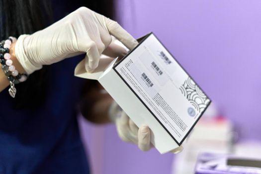 Close up view of the hands of a female doctor with sterile gloves removing medication from a box