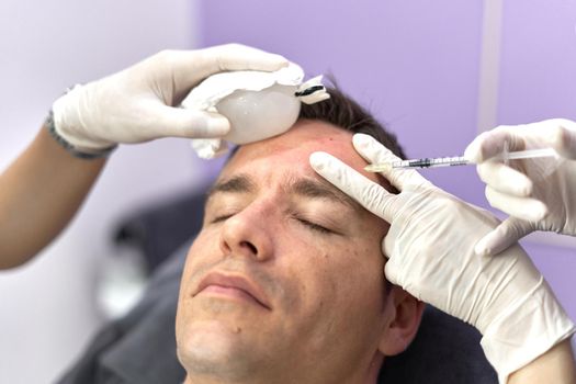 Staff at a beauty treatment clinic applying ice to a man's face while he receives a botox injection