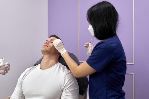 Doctor cleaning the area where she will inject a vaccine of botox for a beauty treatment to a man