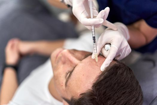 Man sitting in a clinic receiving a vaccine of collagen in the forehead for a beauty treatment