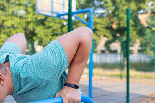 A man is exercising on the street. Training for beautiful hands. Opening gym outdoors on the sports ground in a green park