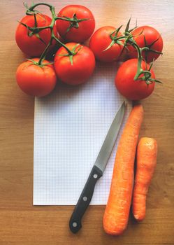 tomatoes and carrot on a wooden background with sheet of paper and knife