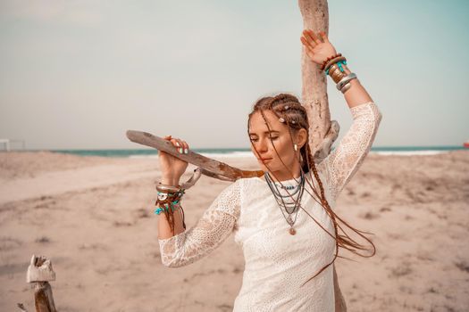 Model in boho style in a white long dress and silver jewelry on the beach. Her hair is braided, and there are many bracelets on her arms