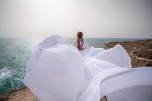 Happy freedom woman on the beach enjoying and posing in white dress. Rear view of a girl in a fluttering white dress in the wind. Holidays, holidays at sea