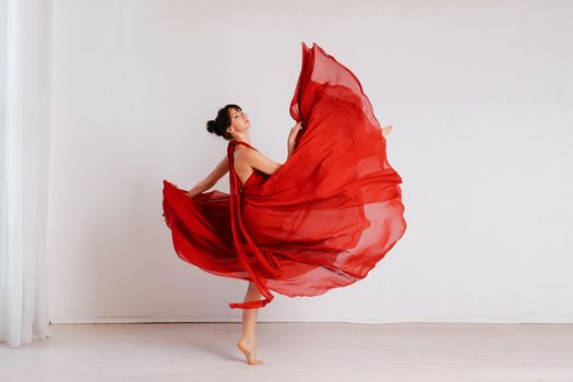 Dancer in a red flying dress. Woman ballerina dancing on a white studio background.