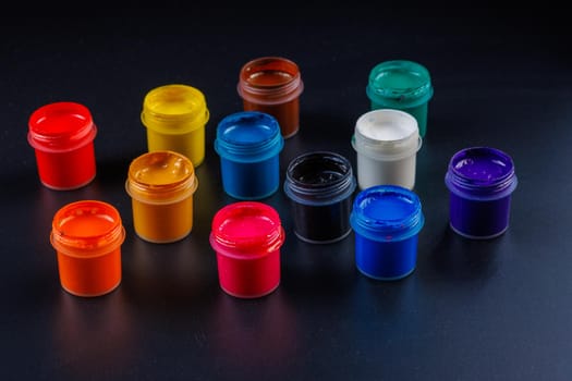 close-up background of opened small gouache paint jars on flat black surface