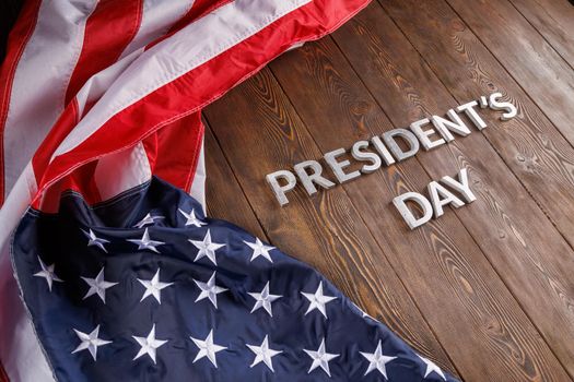 words presitdents day laid with silver metal letters on wooden surface near crumpled US flag