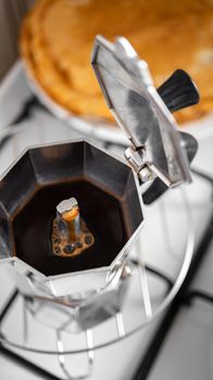 Coffee preparing in moka pot with pancakes at the background. Brewing coffee at home using italian kettle of stainless steel.