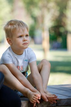 A portrait of a sad little boy in a summer park, a child worried, his eyes full of tears.