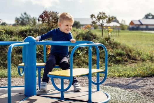 Caucasian boy spins on a children's carousel on a children's walking area in the city. The boy is happy and smiles.