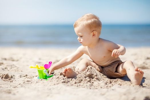 Boy plays in the sand on the beach near the sea. The child is focused and he likes his toys