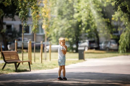 A little boy is standing in the shade of trees in a city park, the child is alone he is afraid of getting lost.