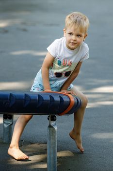 Portrait of a little boy in an outdoor sports gym, a child performs gymnastic exercises barefoot on modern equipment.