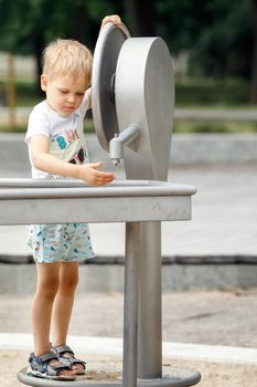 A happy little boy plays with a water tap in a city park. Special water equipment for children's games on a hot summer day outdoors. Vertical photo.