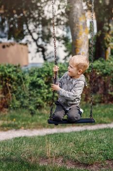 Cute young boy having fun on a swing in sunny summer park. Family weekend in a city.