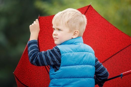 Close up portrait of boy in blue raincoat hold umbrella in the rainy day.