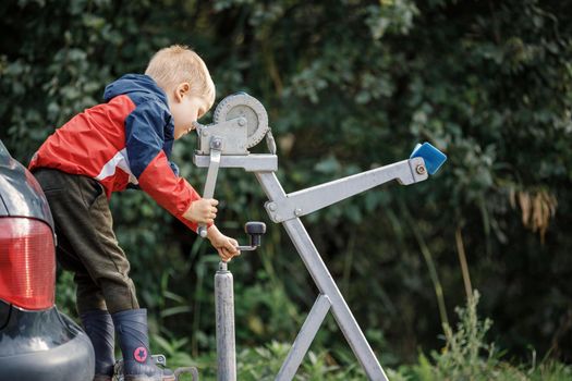 A curious little boy works with a winch on a trailer. Moving heavy loads, loading and unloading motor vehicles and boats.