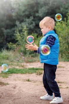 The little boy catches soap bubbles in autumn nature.