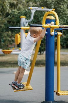 The little boy swings and perform exercises on an outdoor gym equipment.