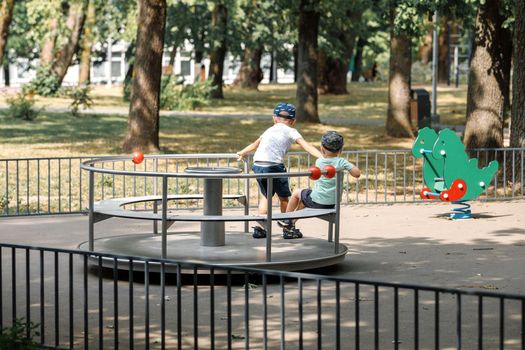 Two little boys are turning on the carousel on the playground.