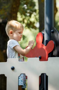 A cute, hilarious, blond boy plays on an outdoor playground, he drives a pirate ship.