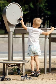 Barefoot little boy wearing shorts and t-shirt playing with water pump faucet in public park.