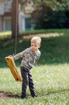 A broken swing in a city park and a cute boy who can't swing.