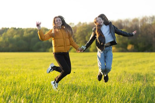 Mom and daughter casual dressed jump in field at beautiful spring sunset. Mothers love concept.