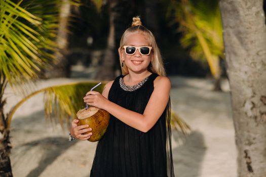 Portrait of a cheerful 9-year-old girl with a coconut cocktail on the background of palm trees on an exotic beach.little Girl with a coconut on the beach of the island of Mauritius.