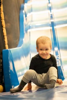 Little toddler boy sliding on shiny metal slide in amusement park at shopping mall