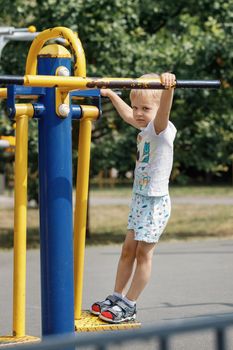 The little boy is training on an outdoor gym equipment.