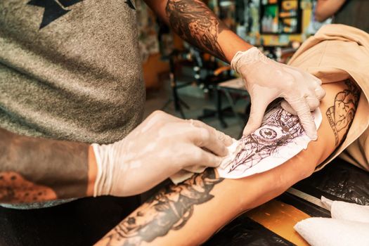 Closeup of a Latino tattoo artist wearing medical gloves putting a sketch of a tattoo on his client's leg in his studio in Managua Nicaragua