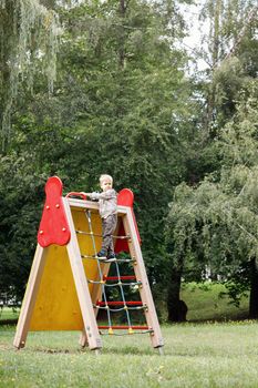 Child climb on rope net in city park. A brave child climbs up to the top.