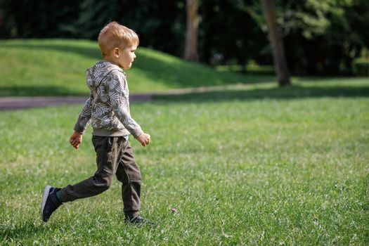 Summer, childhood, leisure and people concept - happy little boy running on green field outdoors.