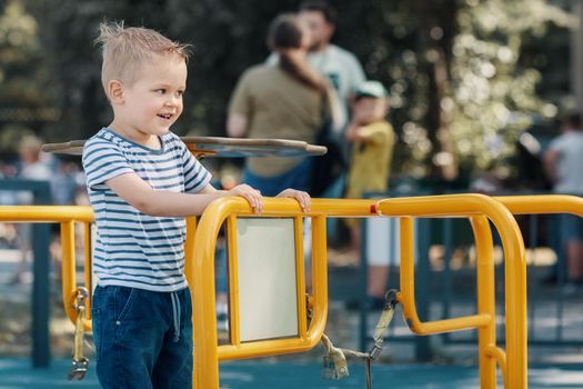 A little smiling boy in a playground on a yellow carousel.