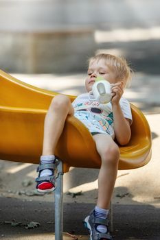 The little boy slips into a yellow plastic slide, his hair becomes eclectic, child sits down comfortably to calm and drink.