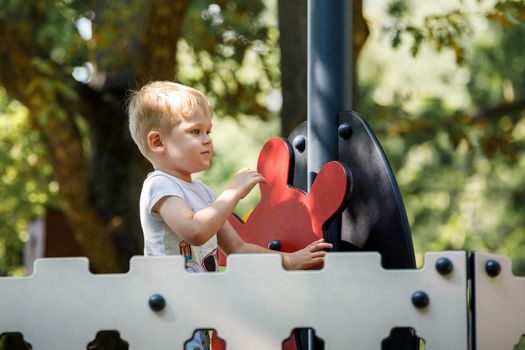 The brave little boy plays the captain of the ship, he turns the red helm of the ship. Modern, contemporary playground in a green summer oak park.