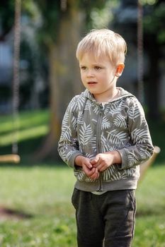 A lonely lost and worried little boy in a summer park. Vertical photo, portrait.