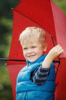 Little boy taking red umbrella with smiling happy face. Vertical photo.