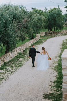 Happy stylish smiling couple walking in Tuscany, Italy on their wedding day. The bride and groom walk down the street by the hands. A stylish young couple walks. Husband and wife communicate nicely. Lovers run through the streets of the city.