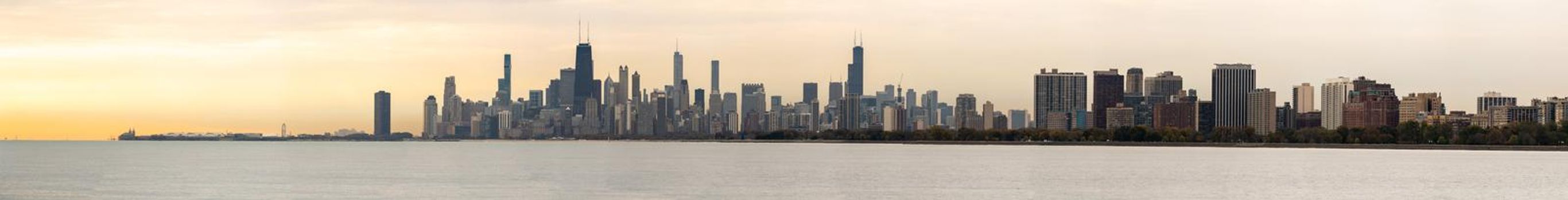 A large panorama of the Chicago Skyline at sunrise with orange clouds in the sky and water below.