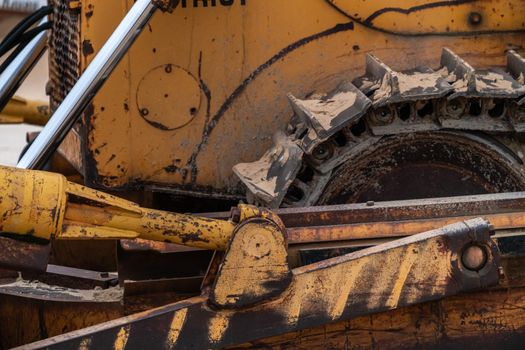 A closeup photograph of the track of an old large industrial yellow bulldozer machine weathered, rusty and worn sitting on a beach in Chicago.