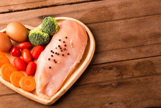 Top view of Raw chicken breasts fillets no boneless with spices rosemary, carrot, and eggs in heart plate wood on wooden background, Healthy food day concept