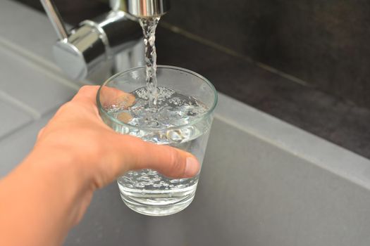 A woman's hand pours water into a glass in a kitchen