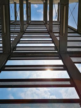 Looking up to metal construction next to block of flat at sunny cloudy day