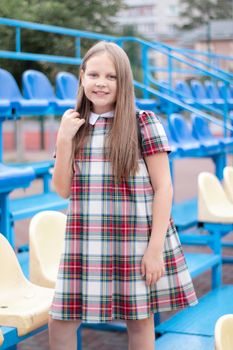 pretty girl in school dress uniform on the blue and yellow tribune of the school stadium. school time. tween