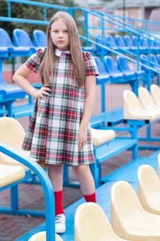 pretty girl in school dress uniform on the blue and yellow tribune of the school stadium. school time. tween