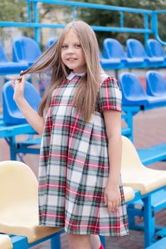 pretty girl in school dress uniform on the blue and yellow tribune of the school stadium. school time. tween