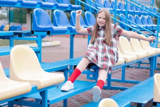 pretty girl in school dress uniform on the blue and yellow tribune of the school stadium. school time. tween