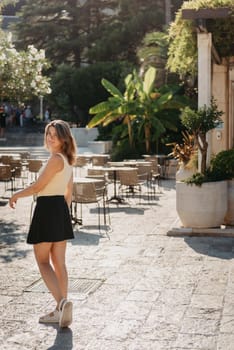 Girl tourist walking through ancient narrow street on a beautiful summer day in MEDITERRANEAN MEDIEVAL CITY , OLD TOWN bUDVA, MONTENEGRO. Young beautiful cheerful woman walking on old street at tropical town. Pretty girl looking at you and smiling